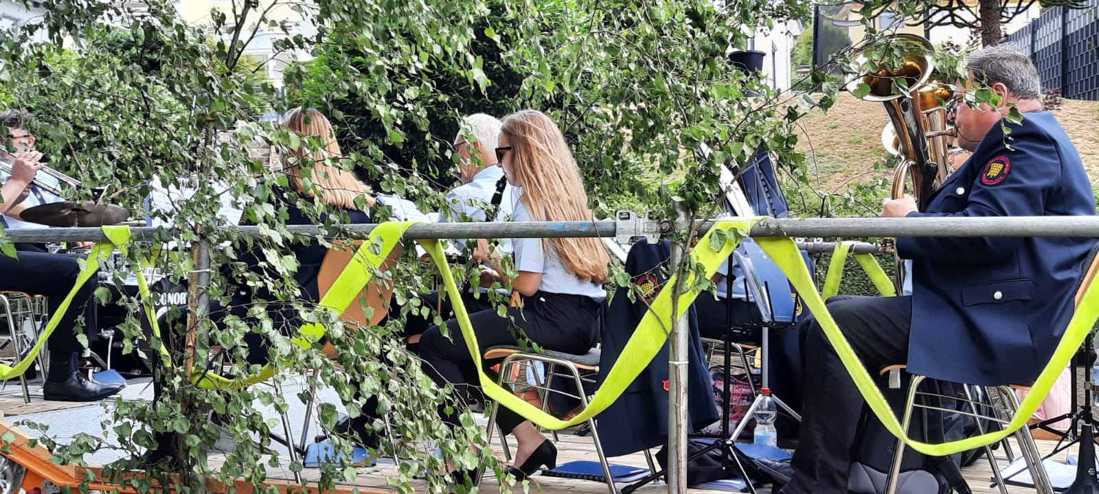 Musikerinnen und Musiker der Kapelle hinter Birkenzweigen auf dem Umzugswagen